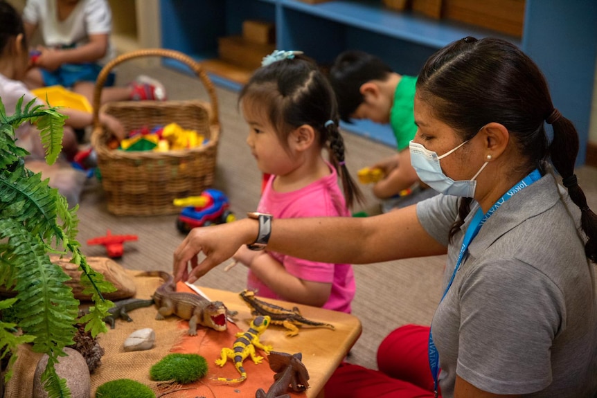 A childcare worker plays with plastic dinosaurs with a young child.