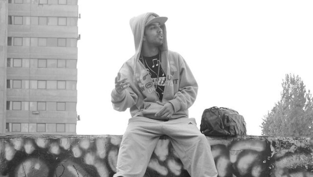 A man wearing a hoodie sits on a graffitied wall.