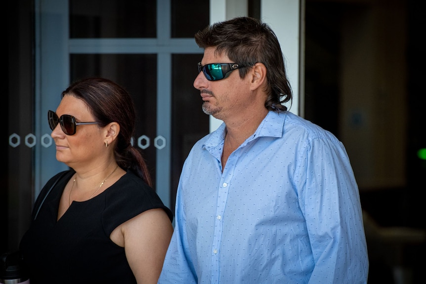 A man with tanned skin and facial hair wearing sunglasses leaves court with a woman