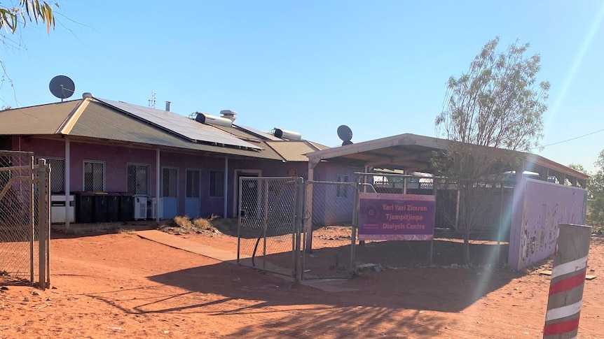 A small blue clinic surrounded by red sand