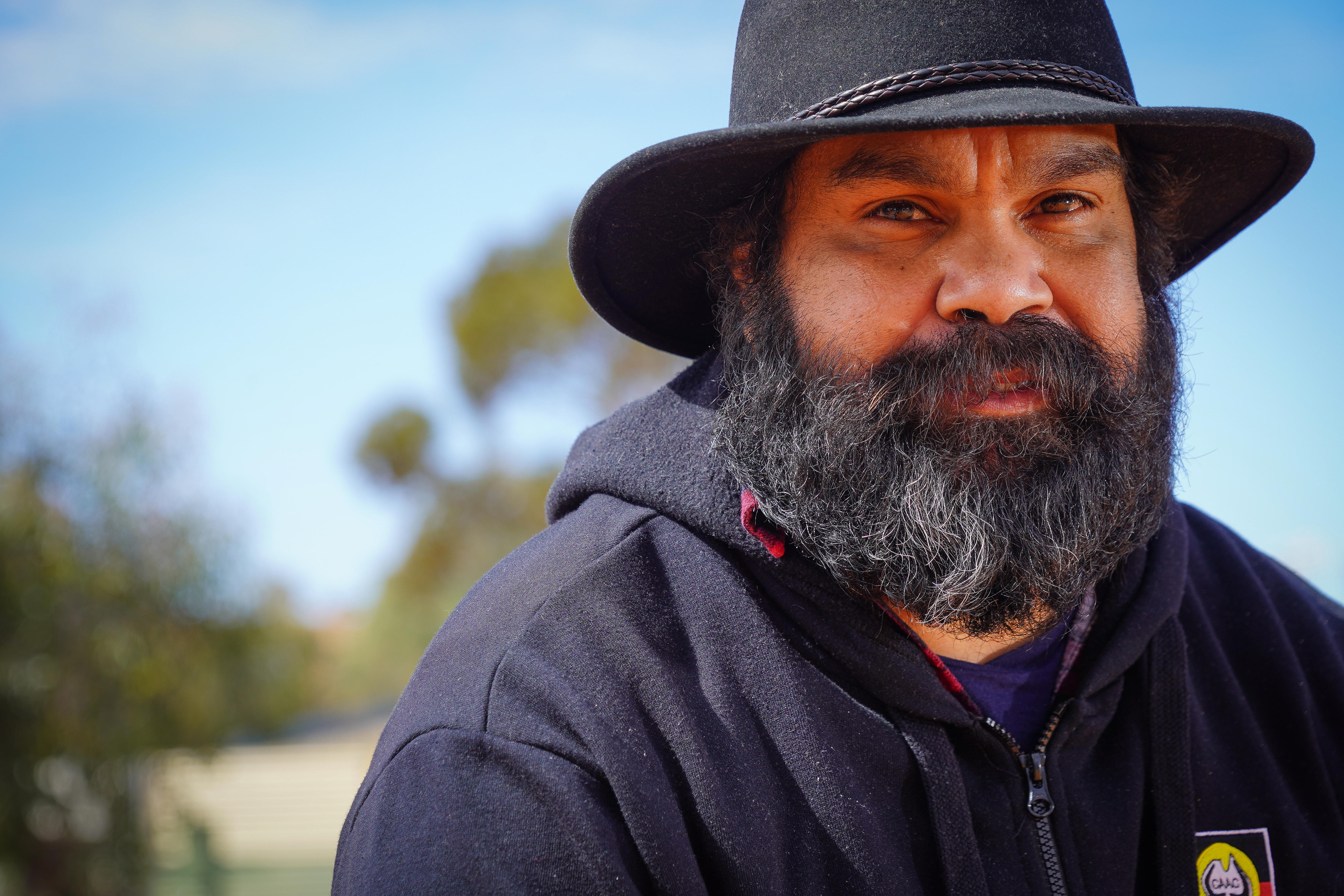 A photo showing a bearded Indigenious man wearing a black hat and looking directly at the camera