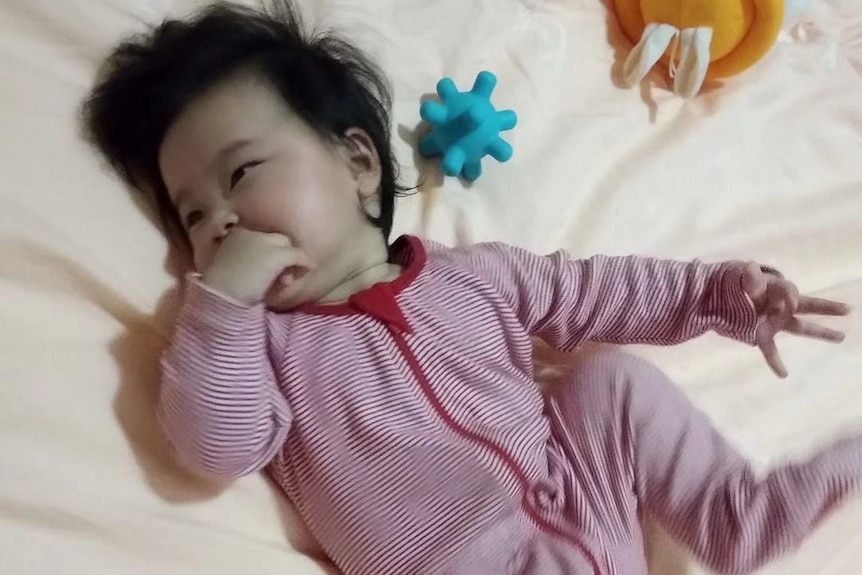 A baby girl lies down in a onesie on a bed.