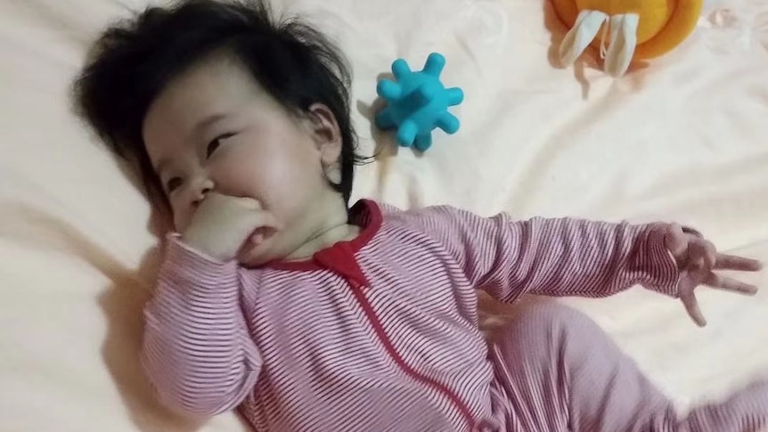 A baby girl lies down in a onesie on a bed.