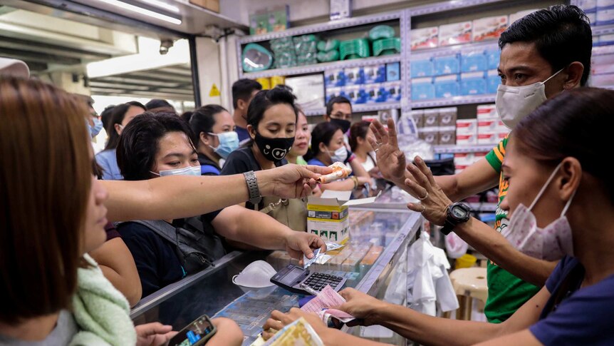 Filipinos swarm around a glass medical cabinet as they try to purchase face masks at a supply store.