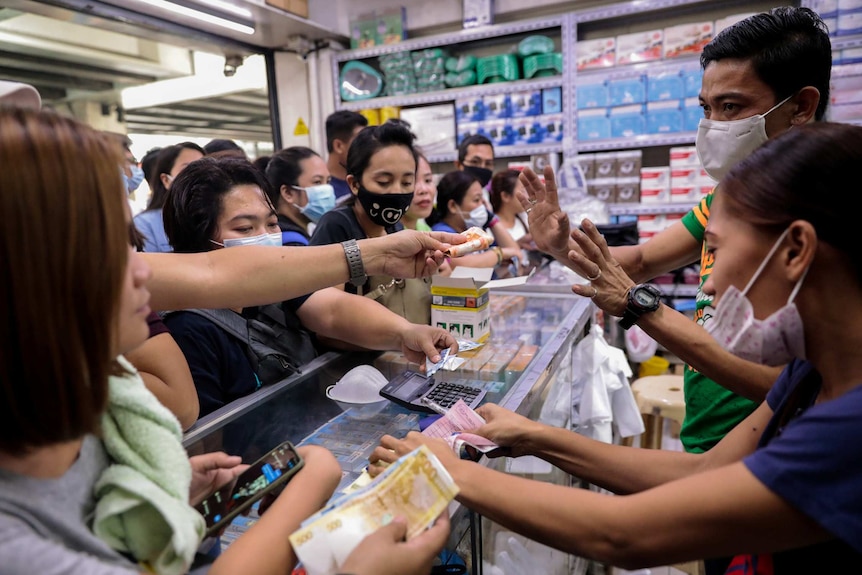 Filipinos swarm around a glass medical cabinet as they try to purchase face masks at a supply store.
