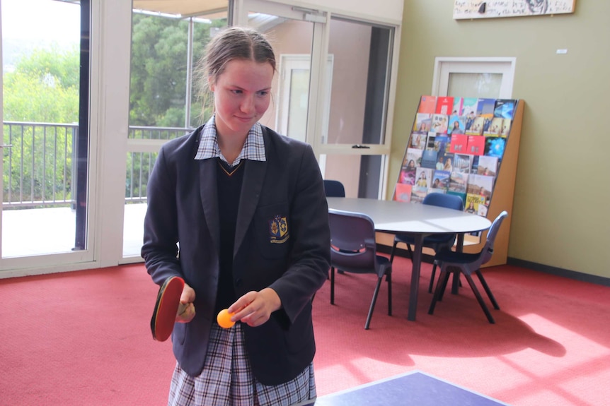 A female student in school uniform prepares to hit a ping pong ball.