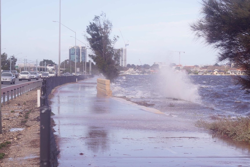 Water sprays up over a footpath next to the freeway.