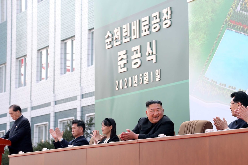 Kim Jong-un sitting with his sister and other advisors in front of a sign with the date on it