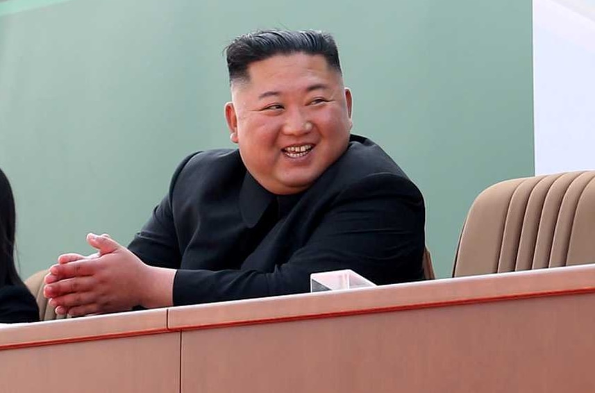 Kim Jong-un smiles as he sits at a long table while others applaud him.