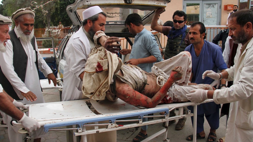 A man whose bloodied clothes have been partly torn away is surrounded by men carrying his stretcher