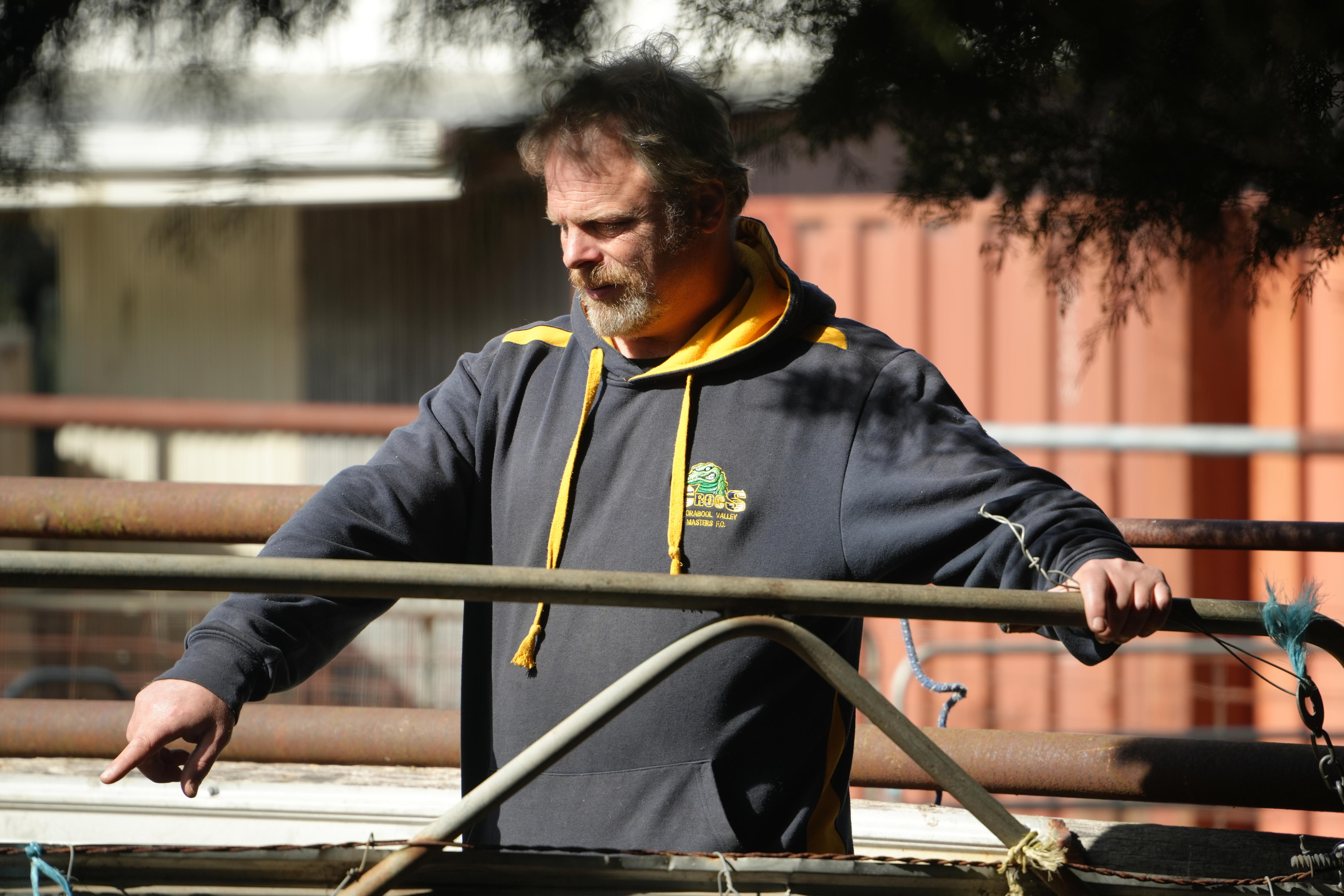 David O'Brien wearing a hoodie while standing in a sheep pen, with one hand resting on a gate and another pointing to something