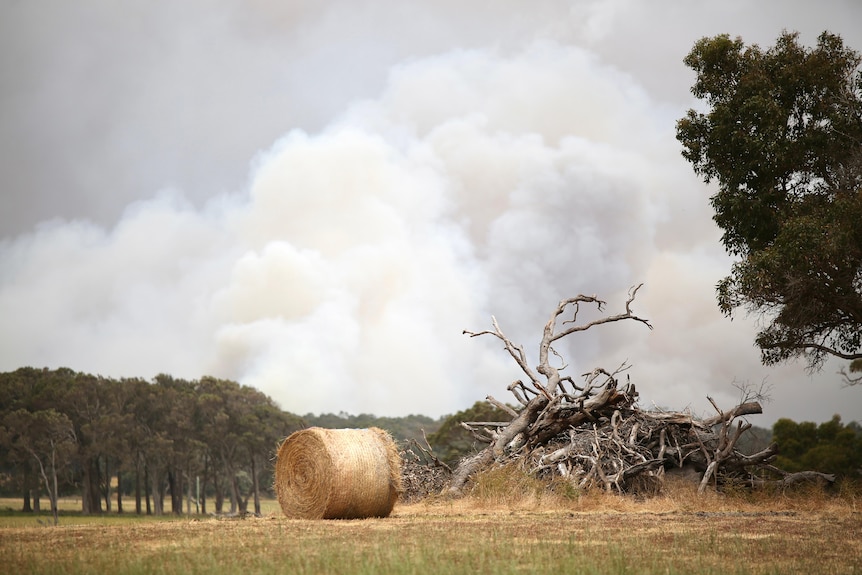 A hay bale and a meadow and smoke in the distance