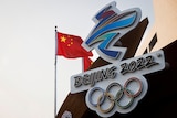 The Chinese national flag flies behind the logo of the Beijing 2022 Winter Olympics.