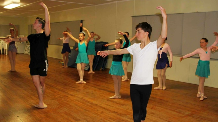 Several dancers following the lead of Queensland Ballet Teacher Callyn Farrell with arms up in fourth position.
