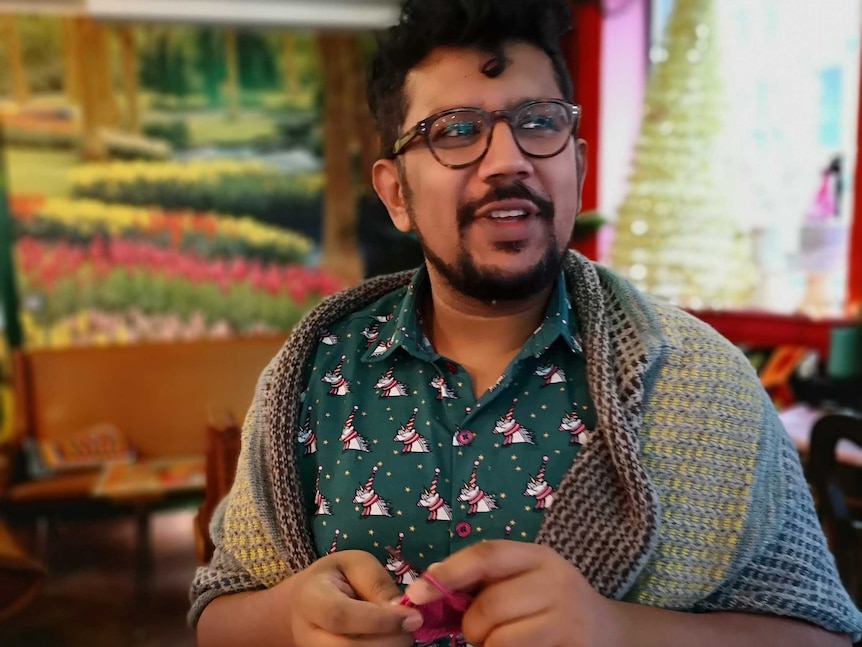 A man looks towards the camera while knitting.