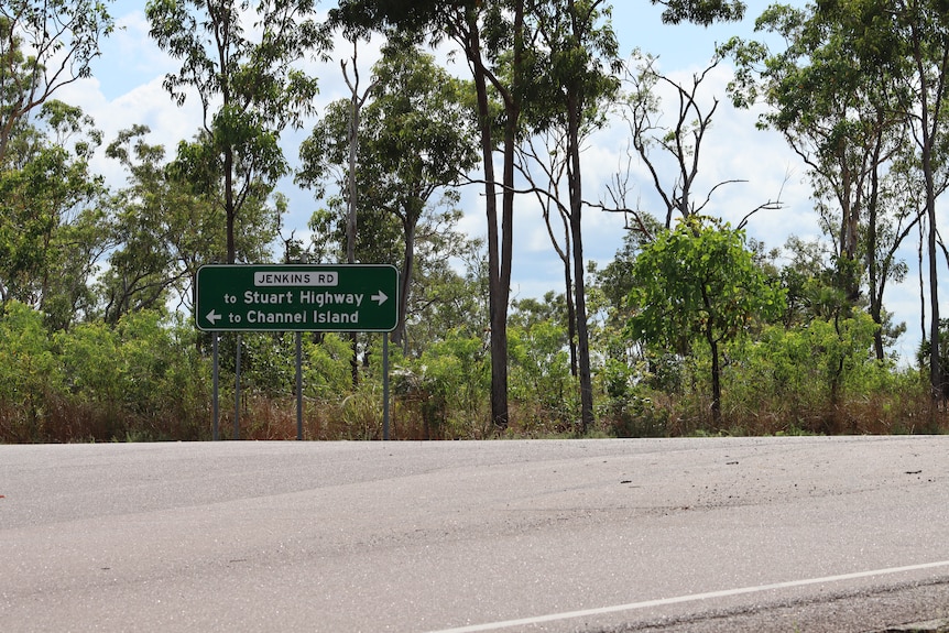 A sign reading 'Jenkins Road' on a section of road bordered by trees and bushes.
