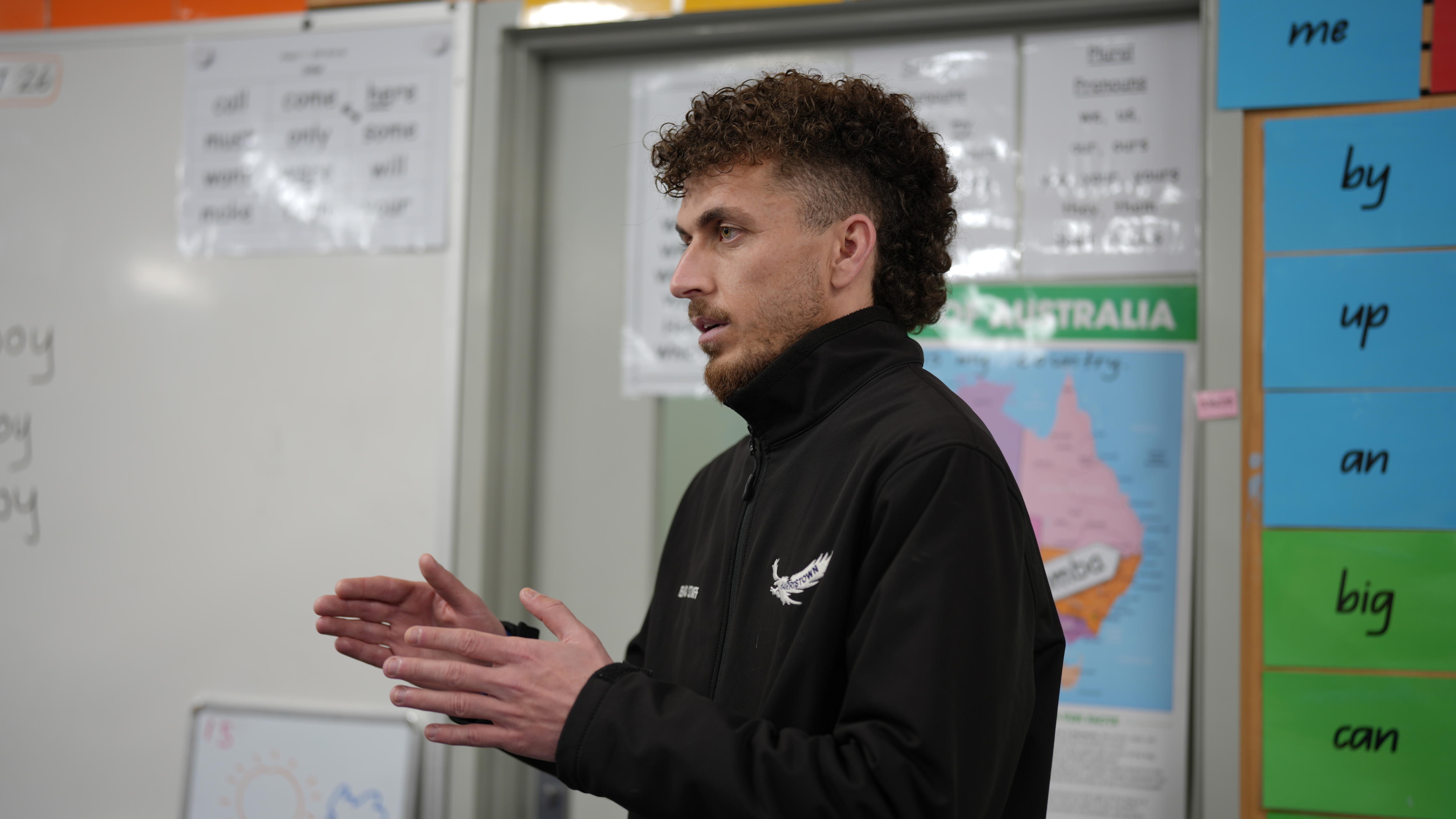 A man with curly hair and a black jacket speaks in class.