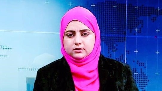 A newsreader wearing a pink hijab and a black jacket.