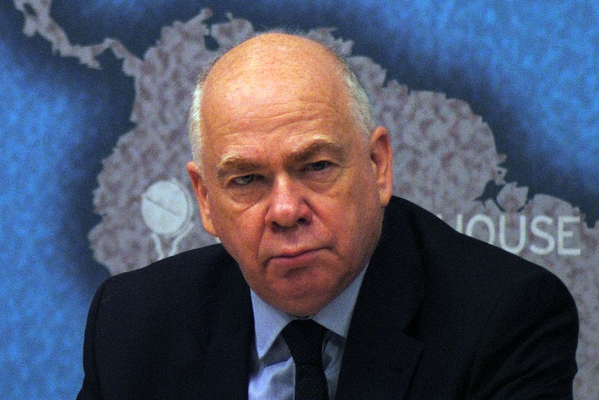 A man sits with a serious expression while giving a talk