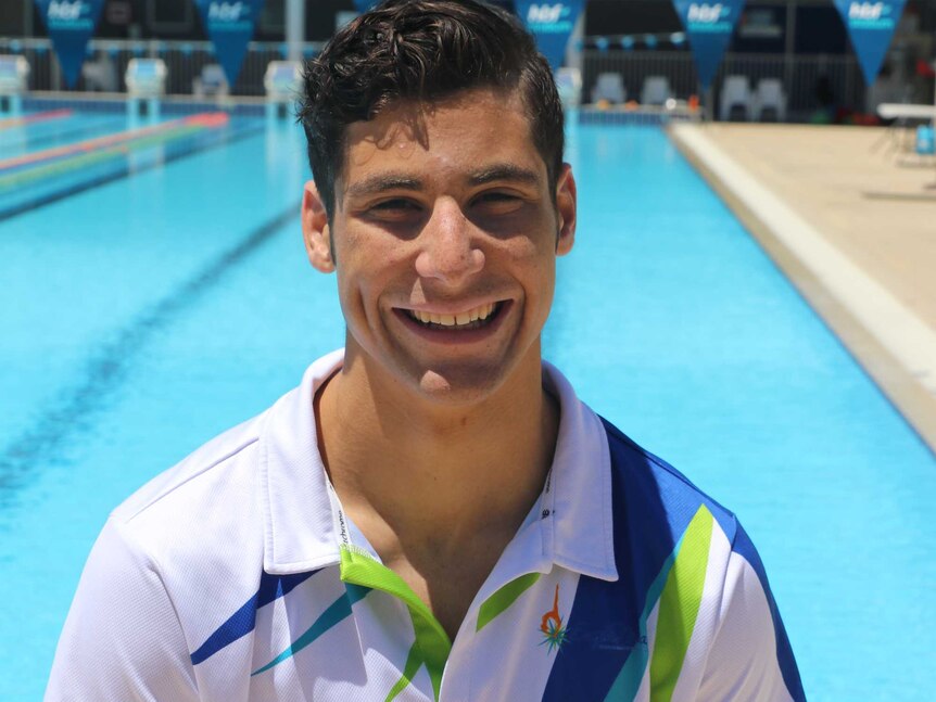 A mid shot of synchronised swimmer Ethan Calleja standing in front of a pool posing for a photo in a polo shirt.