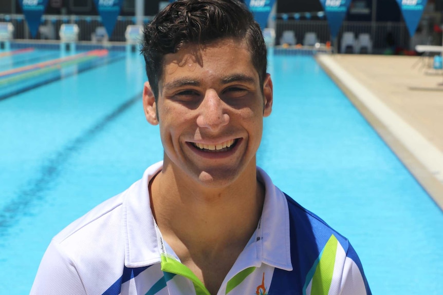 A mid shot of synchronised swimmer Ethan Calleja standing in front of a pool posing for a photo in a polo shirt.