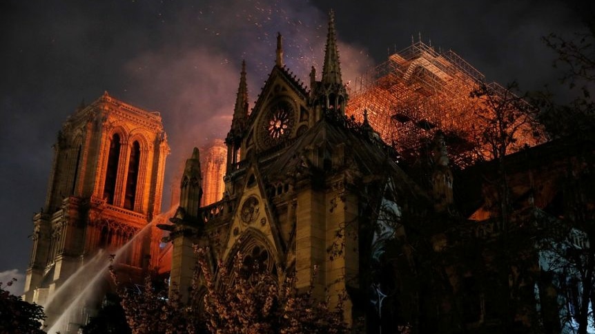 The cathedral lit up by fire, sparks flying and gets of water reaching the roof.