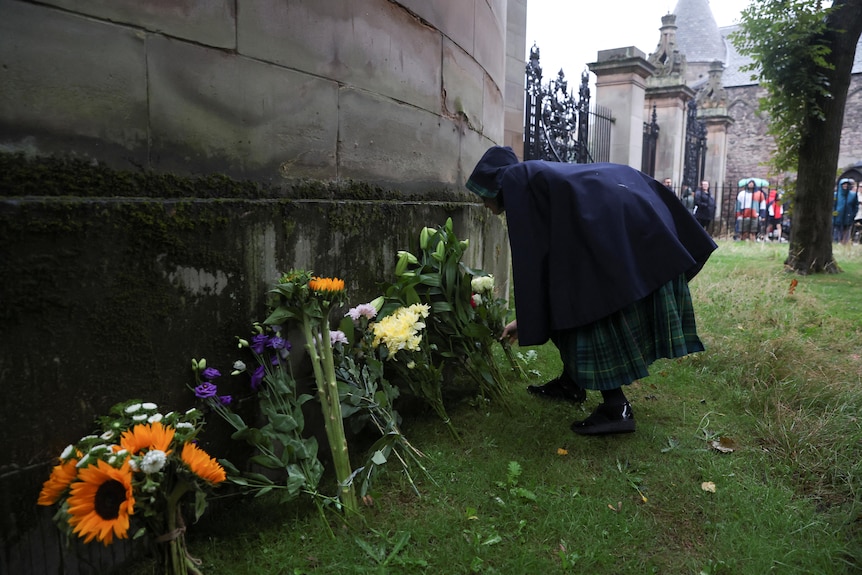 A person placing flowers next to a wall where other bouquets have been placed.