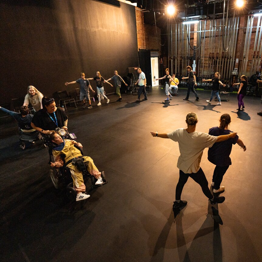 Partners dance in a circle underneath a spotlight on stage