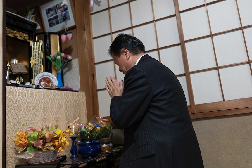Takeshi kneeling in prayer in front of a small shrine