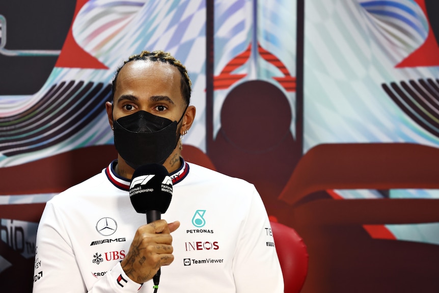 Un piloto de F1 con máscara sostiene un micrófono en una conferencia de prensa.