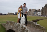 A woman and a man stand on a small stone bridge with a golf bag at their sider