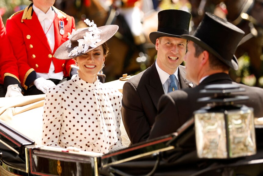 Catherine wearing a fascinator and formal dress sits nex to a formally dressed Prince William on an ornate carriage.