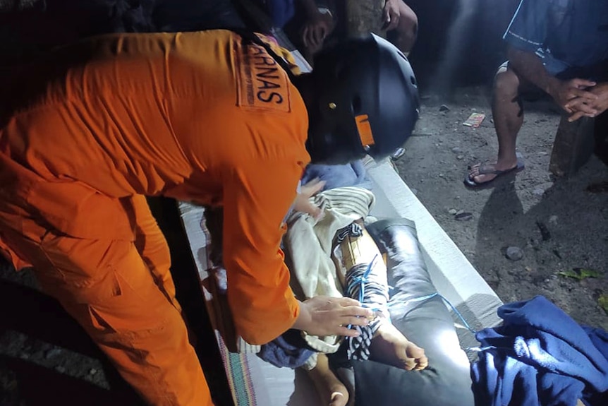 A person in an orange jumpsuit and black helmet leans over a person on a stretcher.