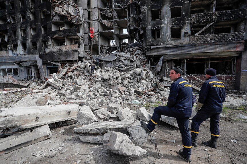 Emergency workers stand and survey a building destroyed by bombing