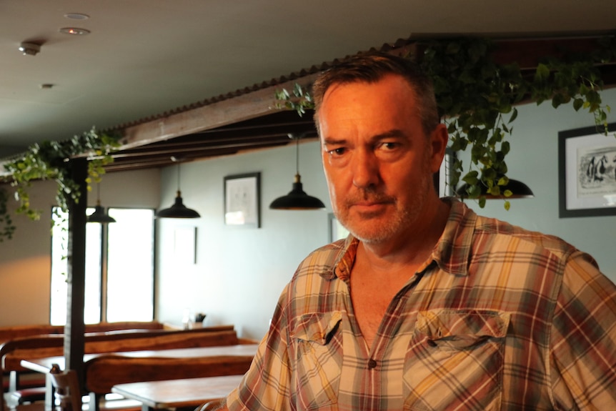 A middle-aged man stands in a dimly-lit bar.