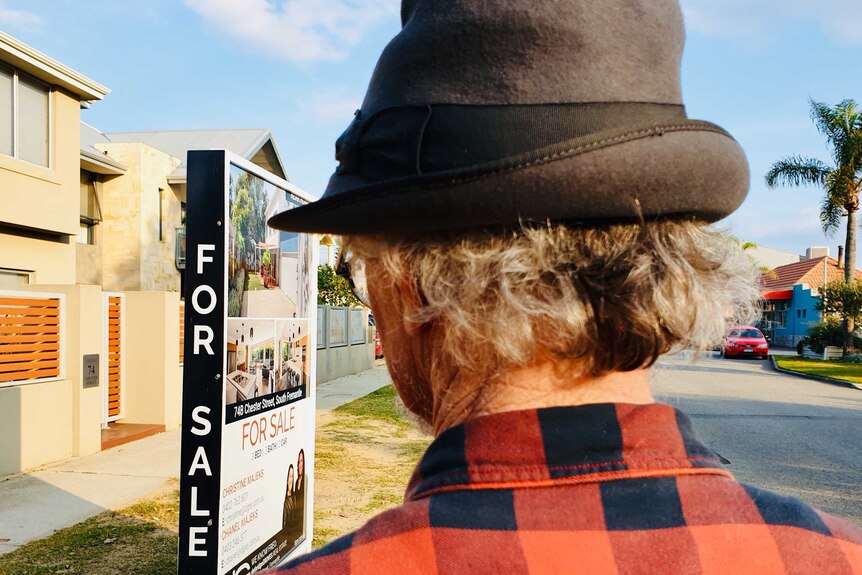 back of man's head, wearing grey hat, looking at for sale sign in street