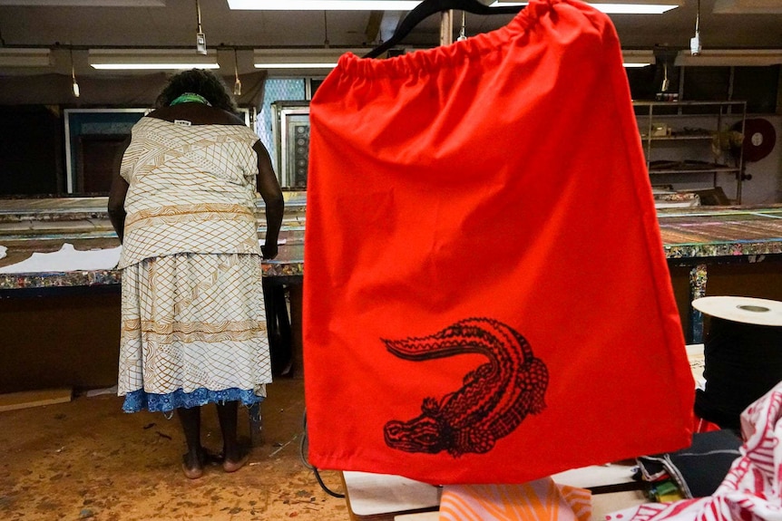 A skirt with a crocodile totem hangs in front of a women working at a bench