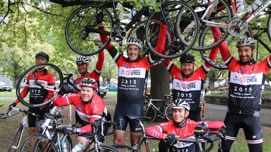 Crew members from Wild Oats XI hold their bikes at the end of a charity ride.