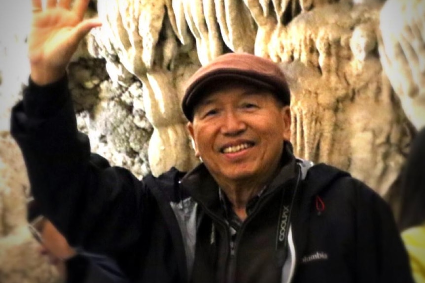 A head and shoulders shot of Australian coronavirus victim James Kwan smiling outdoors and waving a hand in the air.