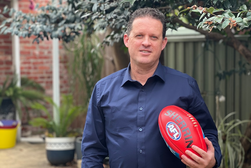 Shane McInerney smiles, holding a red football as he stands in a backyard.