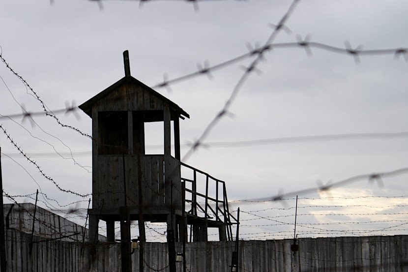 A wooden watch tower surrounded by razor wire keeps watch over the now empty prison yard.