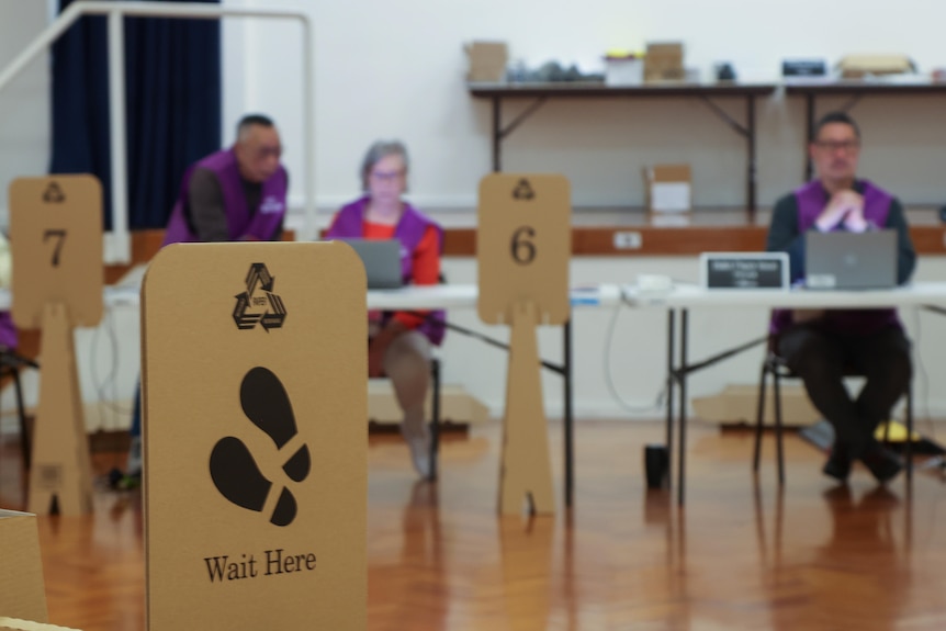 A sign reads 'wait here' inside a pre-polling booth, with electoral staff visible in the background.