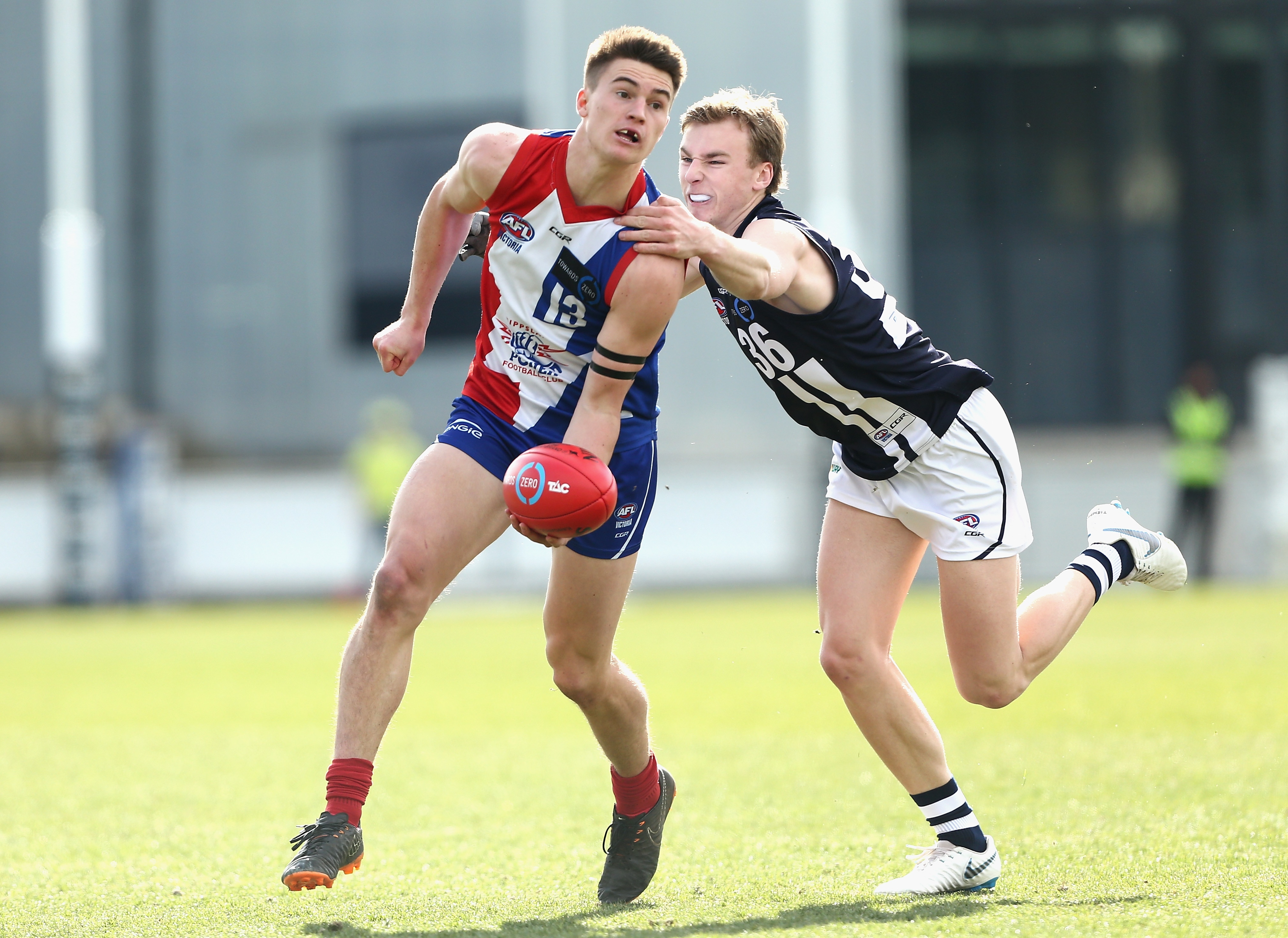 A photo of two AFL players mid-game. One is preparing to handball, the other is grabbing him.