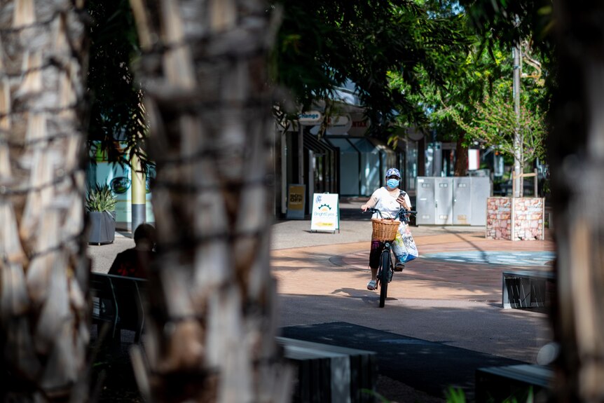 A woman wearing a mask rides a bike down a street in Darwin's CBD.