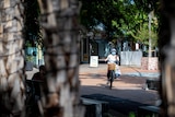 A woman wearing a mask rides a bike down a street in Darwin's CBD.