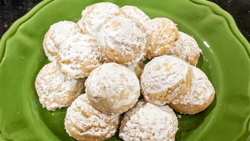 A green plate displays Mexican wedding cookies which are buttery, powdered sugar-covered biscuits.