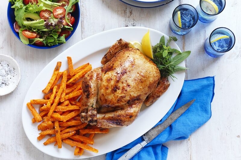 A roast chicken on a plate with chips, salad and glasses of iced water.