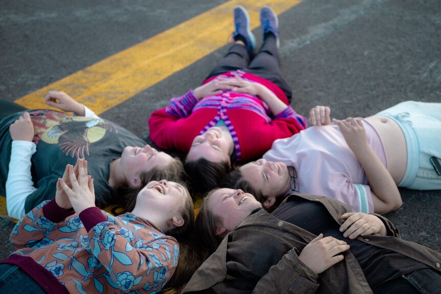 A group of girls lay on the ground in a circle with their heads together and they're looking at they sky