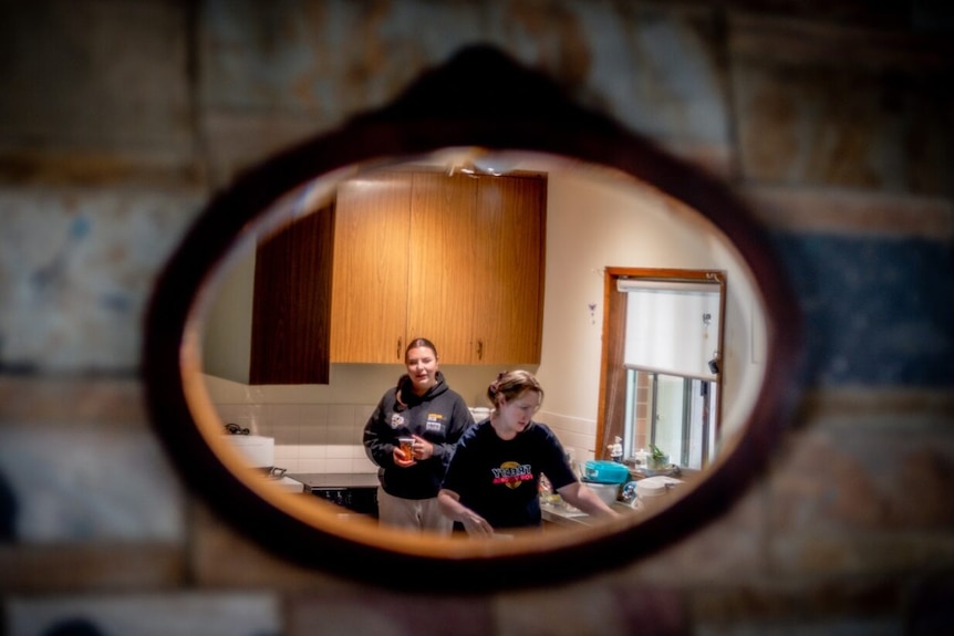 A mirror on the wall showing a reflection of a woman with her daughter in a small kitchen.