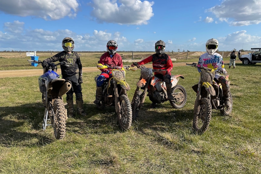 Four dirt bike riders pose for a photograph with helmets on.